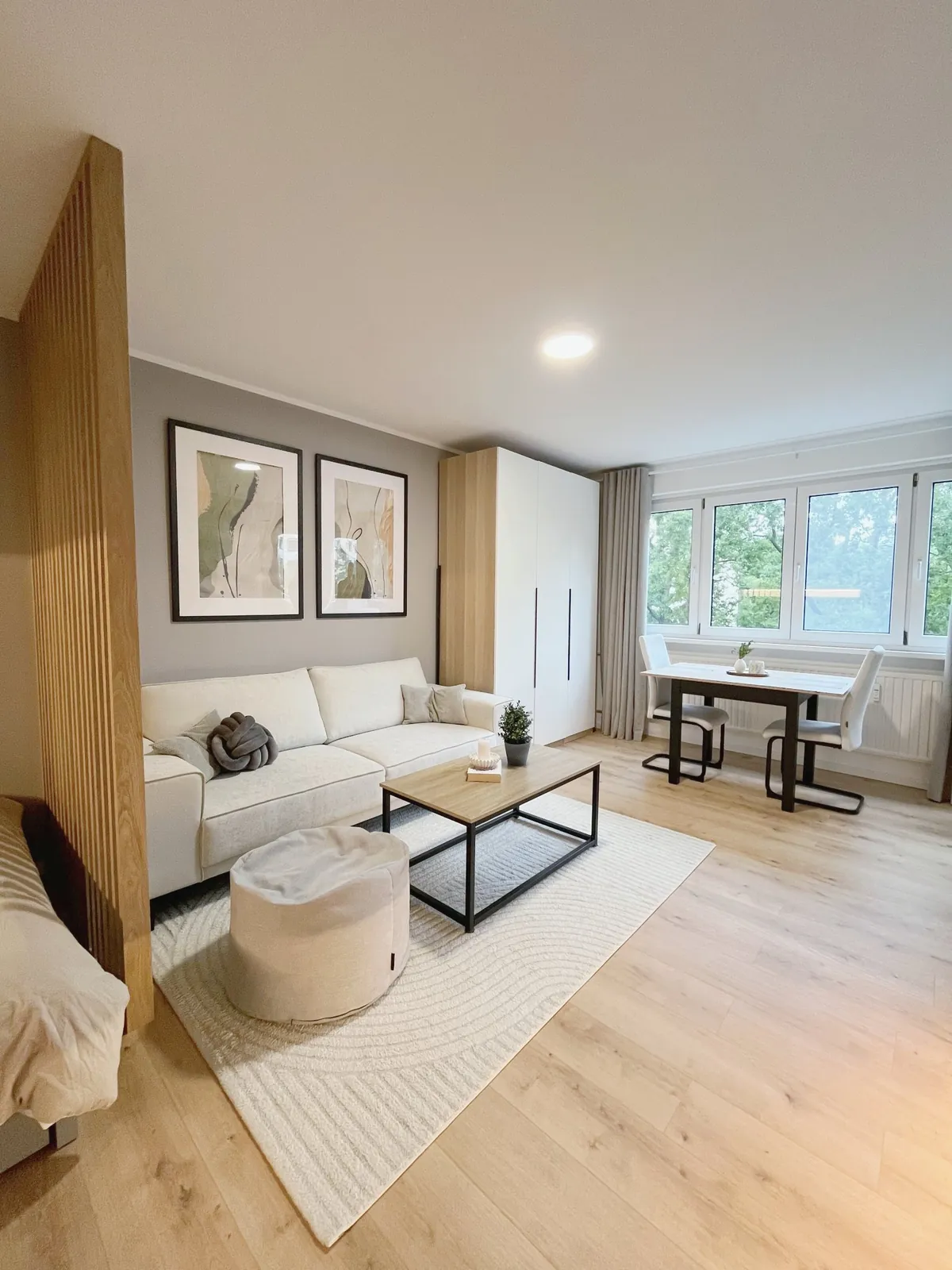 Heller Wohnbereich mit Sofa, Kleiderschrank und Essplatz vor großer Fensterfront